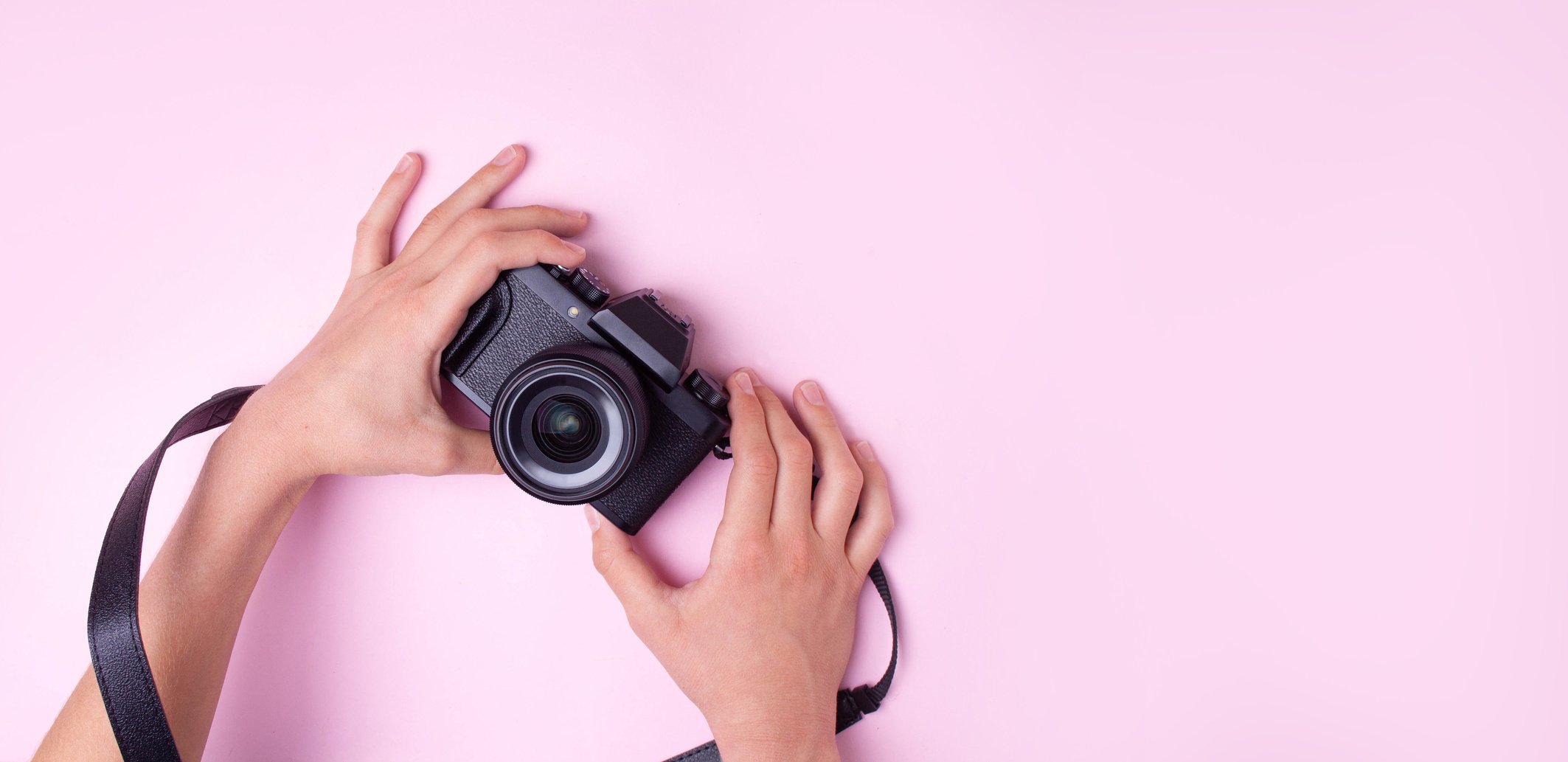 Hands Hold a Black Camera on Pink Background